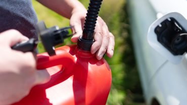 A person refills a car s tank with a red gas can on a sunny day