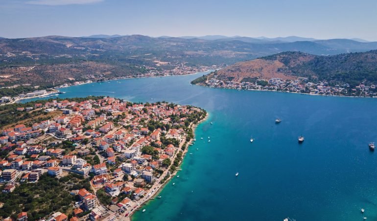 Islands in sea covered with lush greenery and houses, aerial view. Touristic place for summer vacation. Panoramic landscape of Adriatic sea coastline near Rogoznica town in Dalmatian region, Croatia